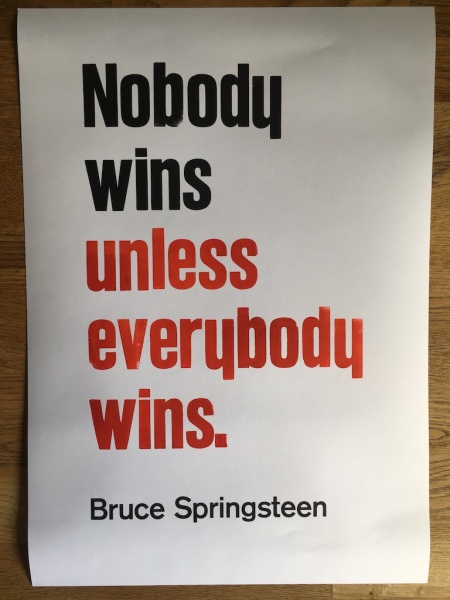 “‘Nobody wins unless everybody wins.’ —Bruce Springsteen” gedruckt in roter und schwarzer Schrift